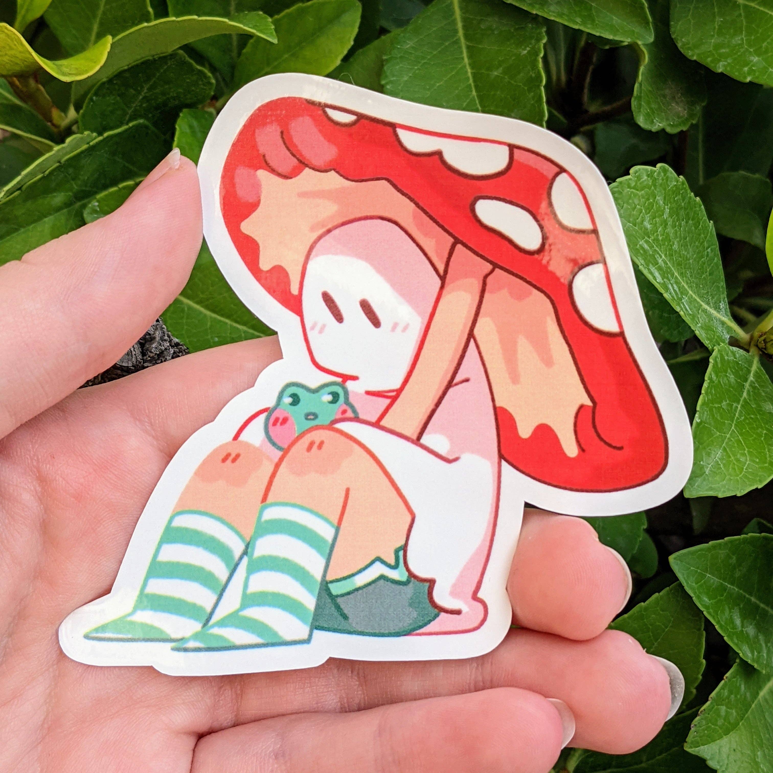 Cute Ghost Stickers : V6 sticker featuring a ghost and frog under a red mushroom with green plants.