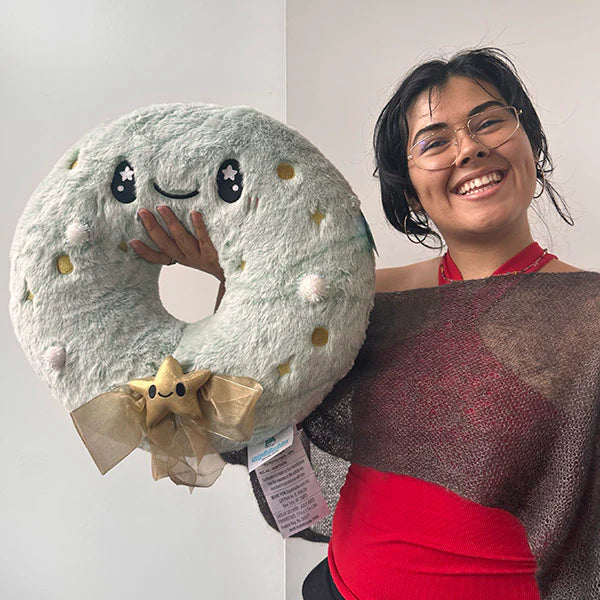 Person holding a Squishable Flocked Wreath pillow shaped like a donut with face and star bow.