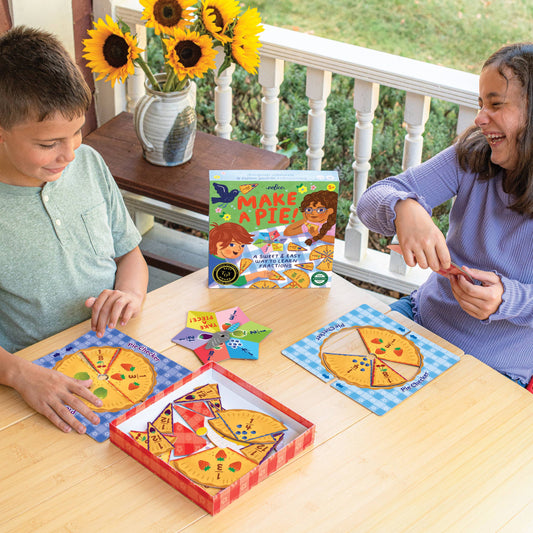 Make a Pie Game, an educational board game about fractions, shown in use by two children at a wooden table.