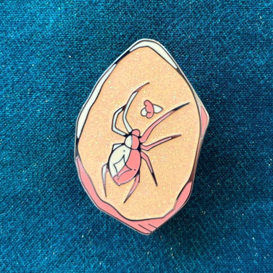 D&D Class Curiosities Pin with spider and heart on a glittery peach background.