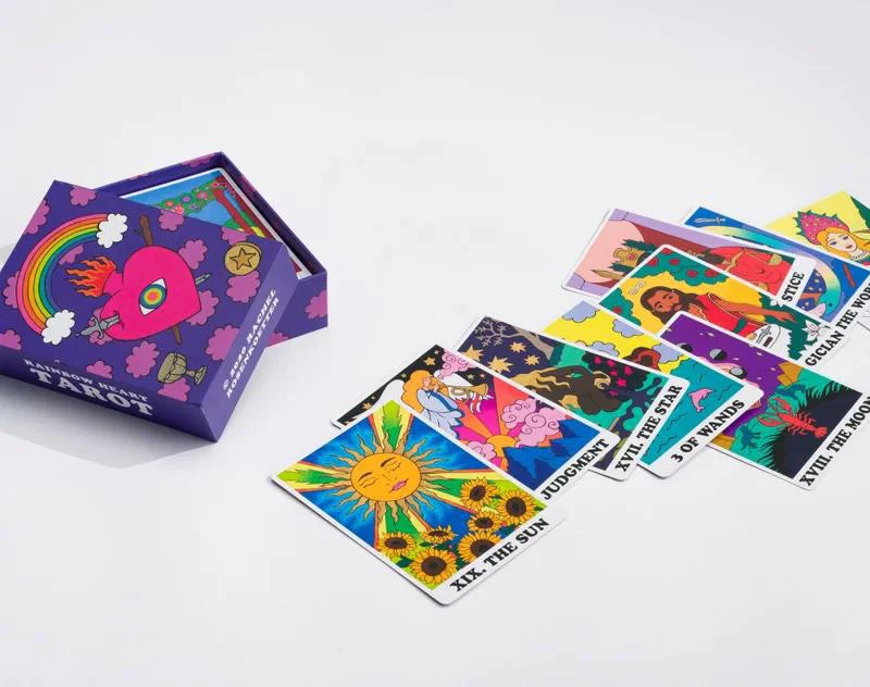 The Rainbow Heart Tarot deck with colorful cards next to a purple box featuring a rainbow and heart design.