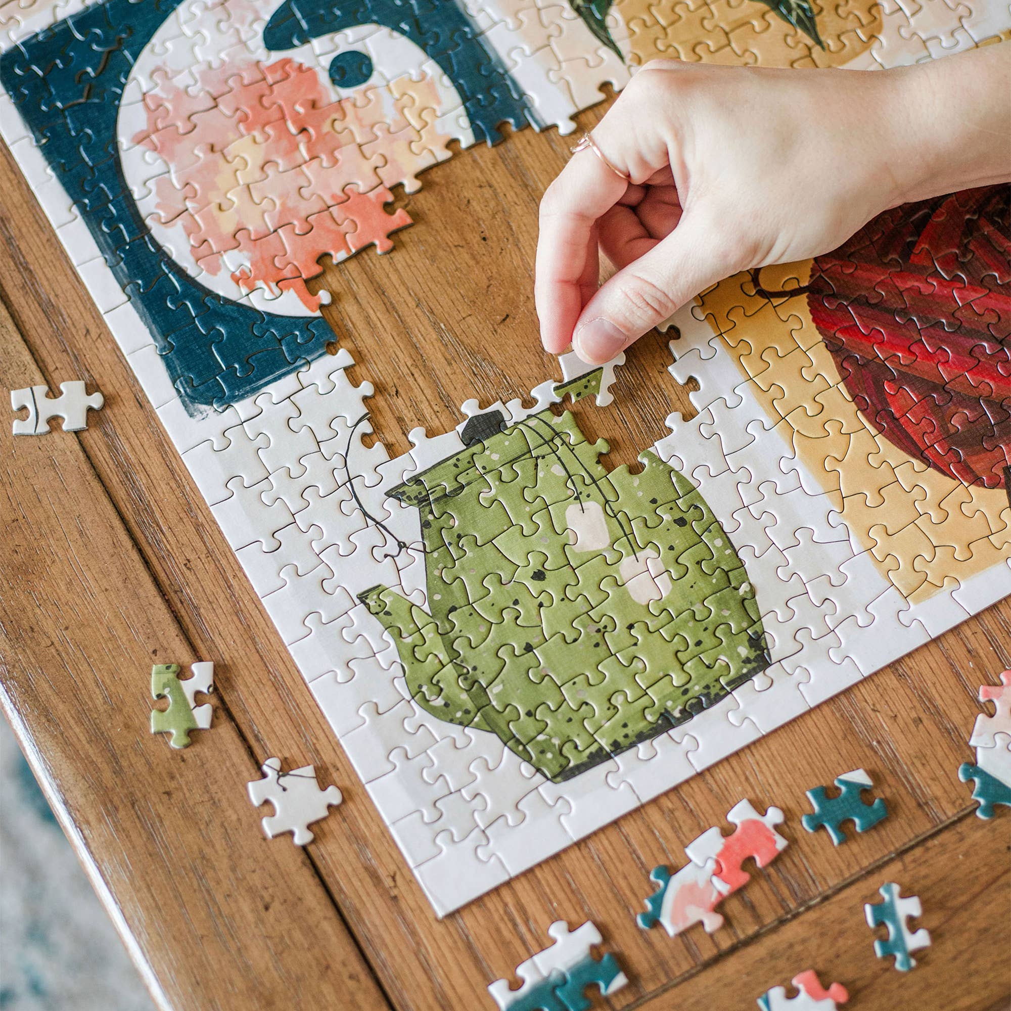 A hand places a piece in the Simple Joys 1,000 Piece Jigsaw Puzzle on a wooden table.