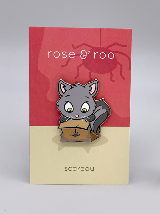 Scaredy enamel pin showing a cartoon gray cat peeking into a box with a spider. Card reads “rose & roo” and “scaredy.”.