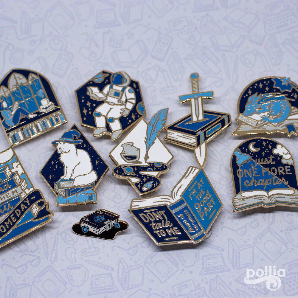 Astronovel Pin with blue and gold enamel, featuring dragon, astronaut, and book designs.
