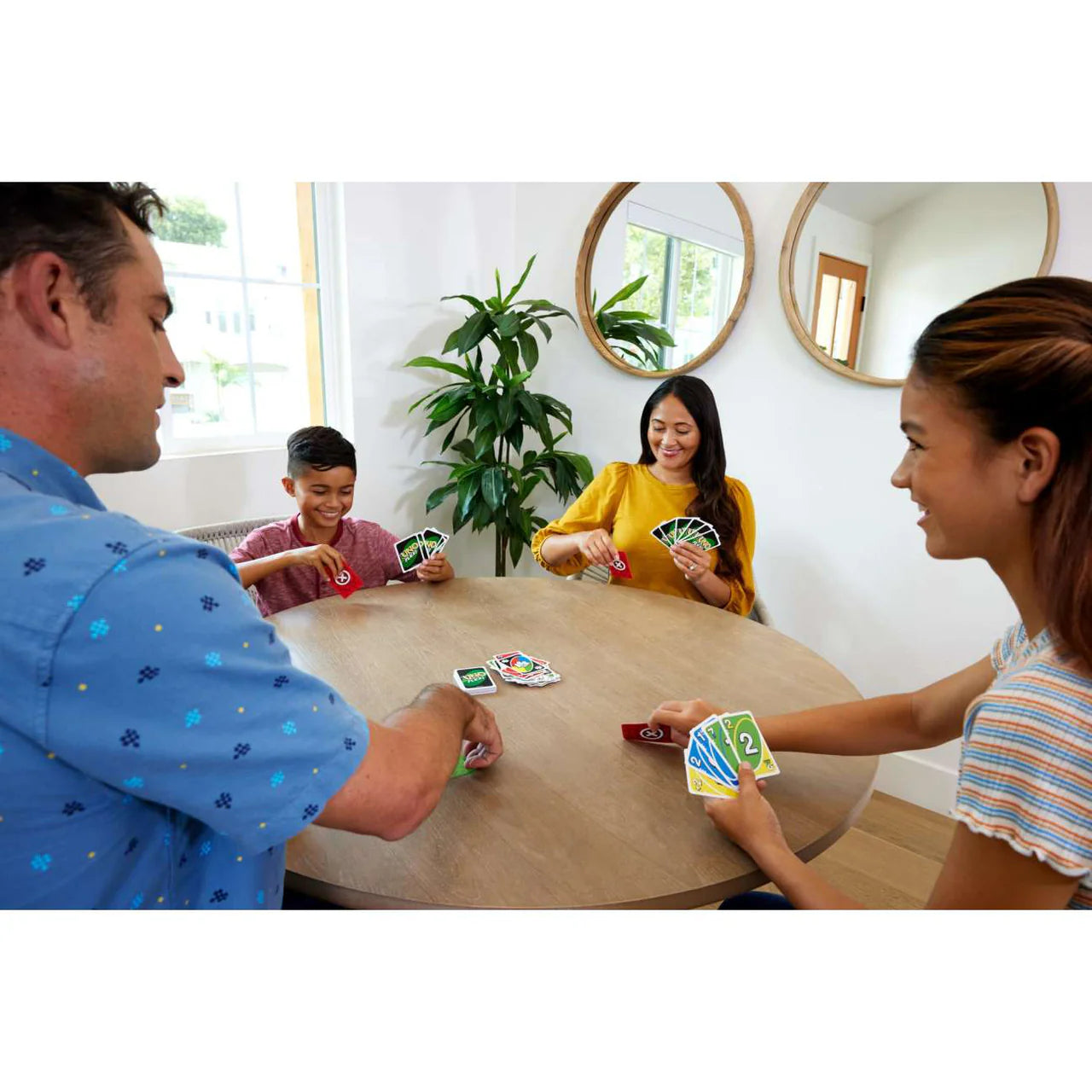 Four people playing UNO Flex card game at a table in a well-lit room.