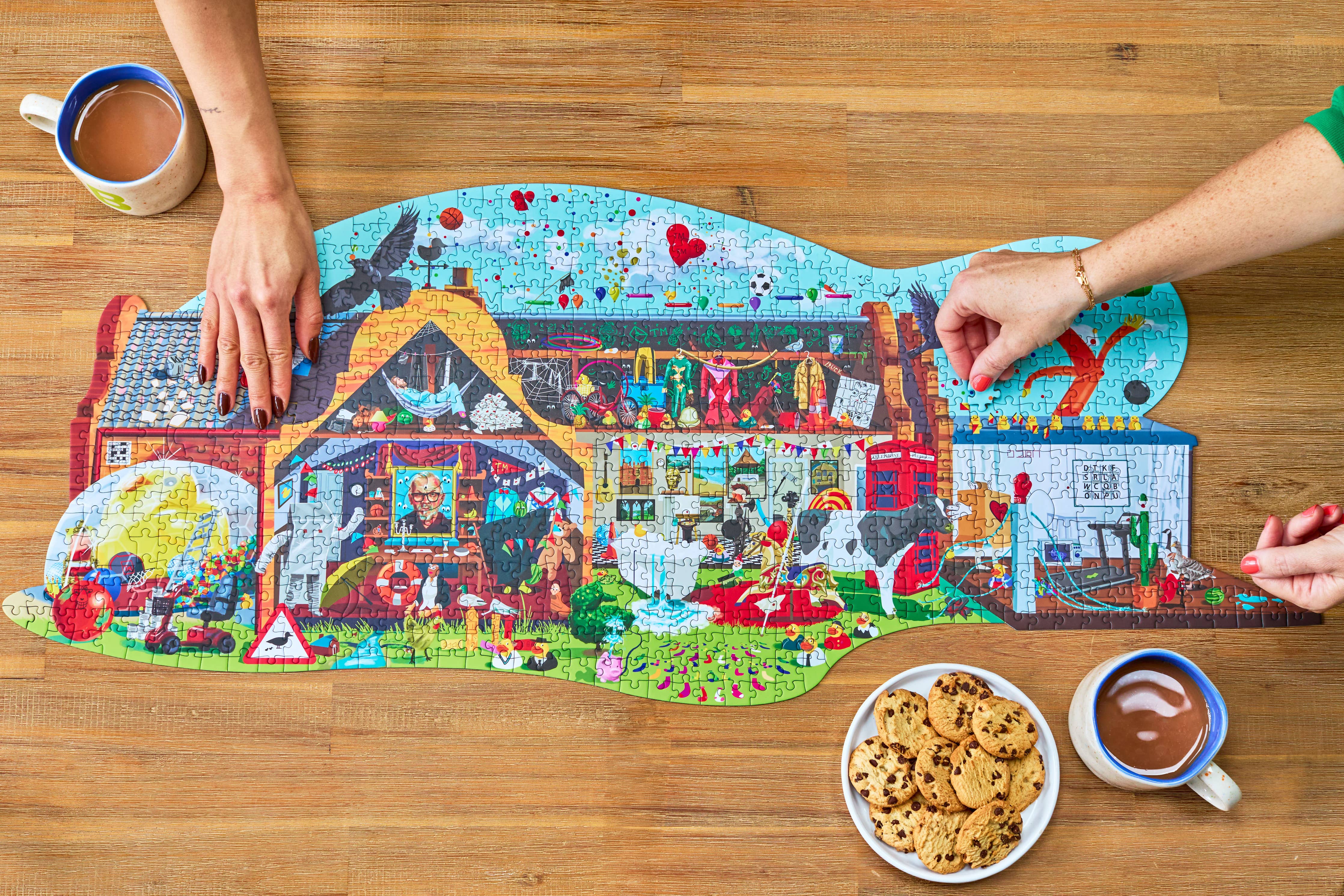 Hands assembling Taskmaster Jigsaw Puzzle (1021 pieces, Secret Task), with mugs of cocoa and cookies next to the puzzle.