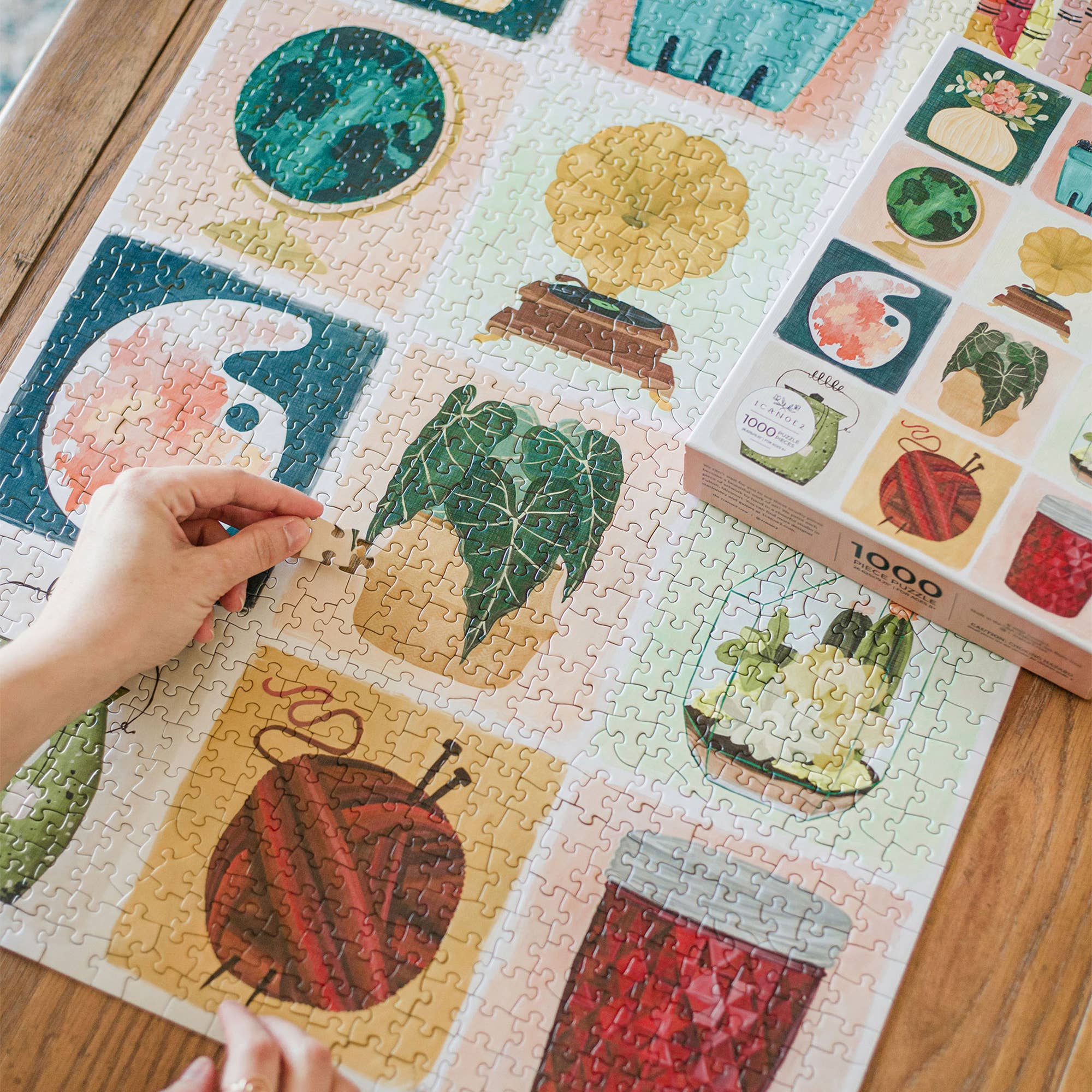 Simple Joys 1,000 piece jigsaw puzzle with hand-painted plants and household objects. A person places a piece.