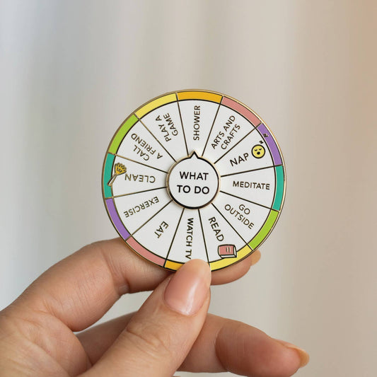 What To Do Spinning Enamel Pin featuring options: nap, meditate, read, and exercise, held in a hand.