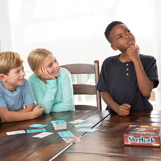 Three children playing Sherlock board game at a table; one boy poses thoughtfully, others smile.
