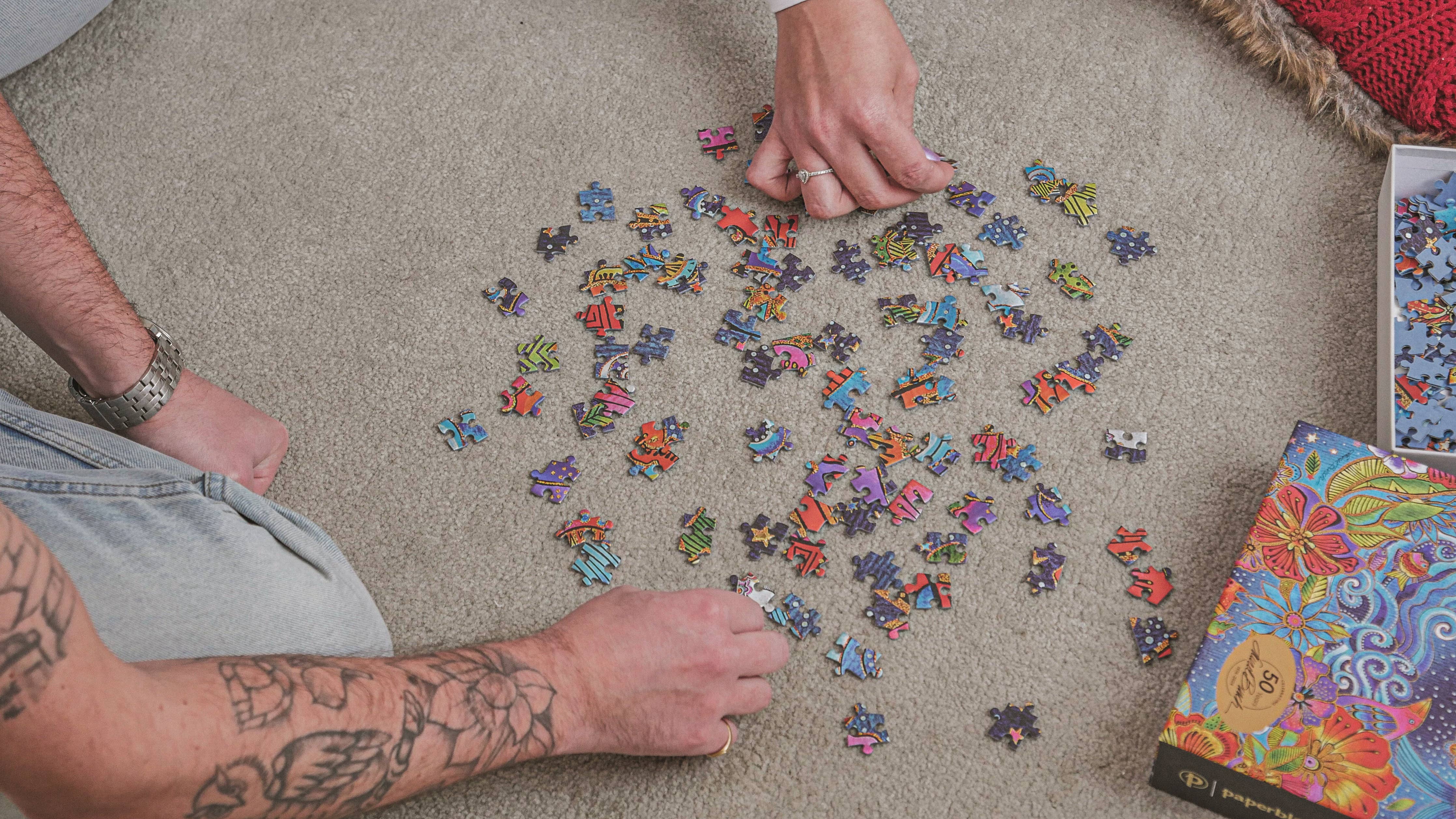 Paperblanks Celestial Magic 1000-piece puzzle pieces and box on carpet, being sorted by two people.