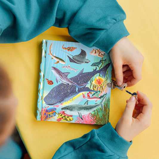 Shark puzzle with ocean theme and Sharks and Friends Journal on a yellow table; person holding a puzzle piece.