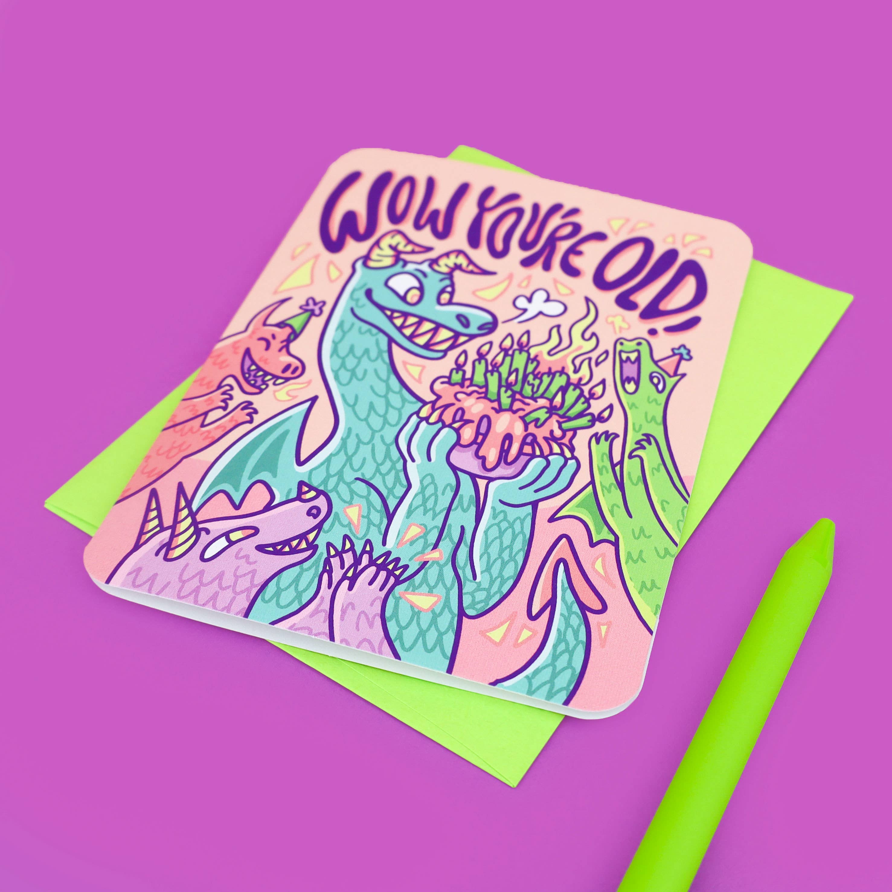 Wow Youre Old Dragon Birthday Card with cartoon dragons and cake, shown with green envelope and pen.