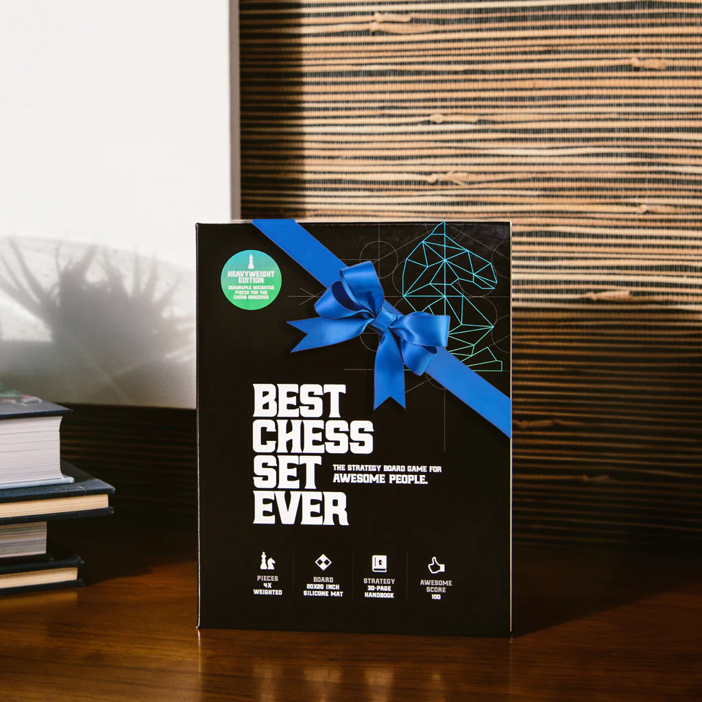 Travel Best Chess Set Ever box with blue ribbon on table next to stacked books.