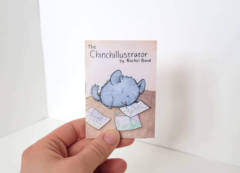 The Chinchillustrator - Mini-Comic Zine by Rachel Bard, a chinchilla comic about artists block, held in one hand.
