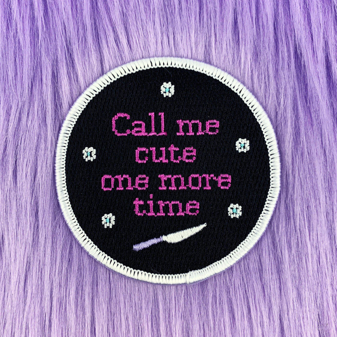 Round Call Me Cute embroidered patch on purple fur, featuring stars, a knife, and the phrase “Call me cute one more time.”.