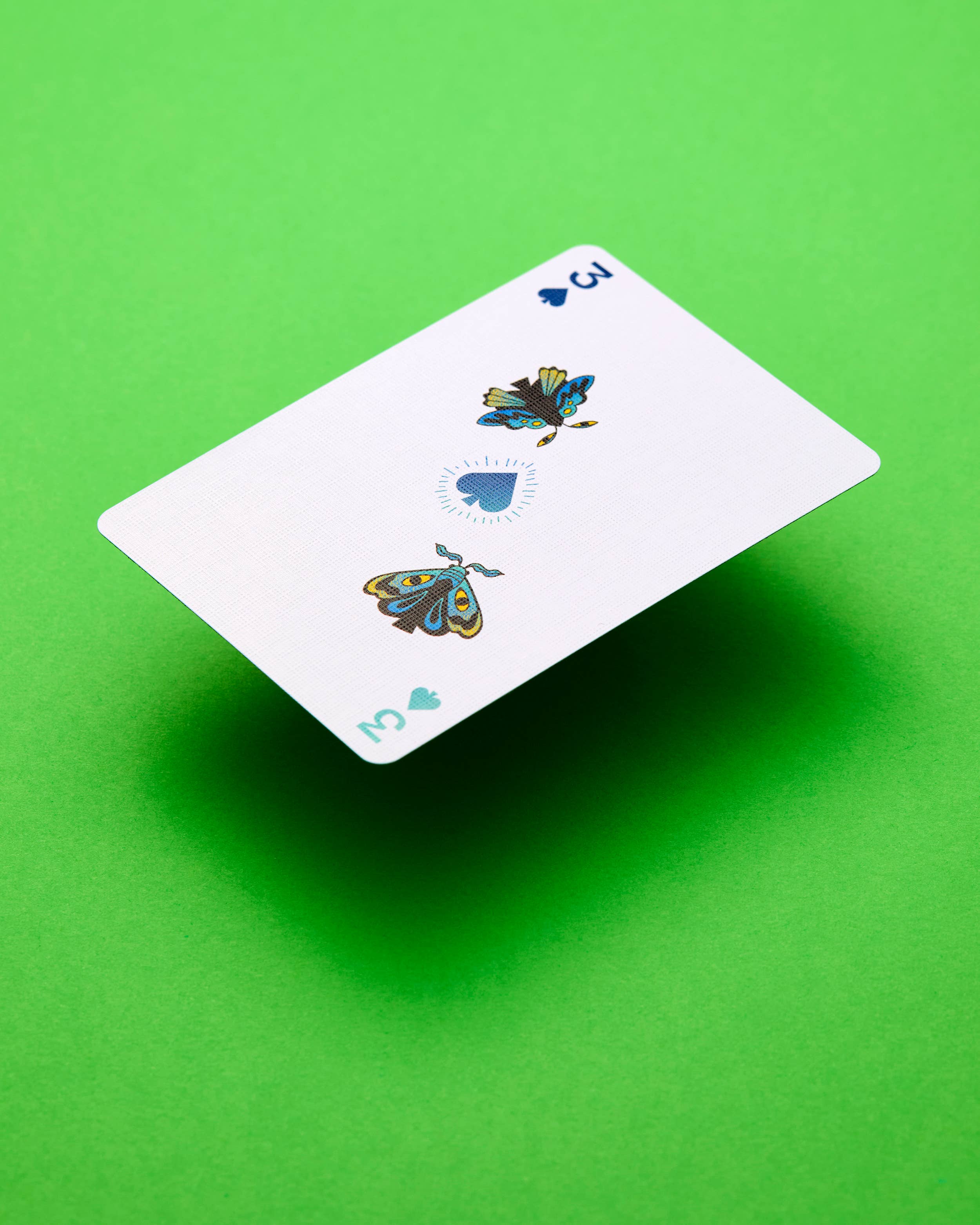 Three of spades from Meow Wolf Playing Cards, featuring moth illustrations on a green background.