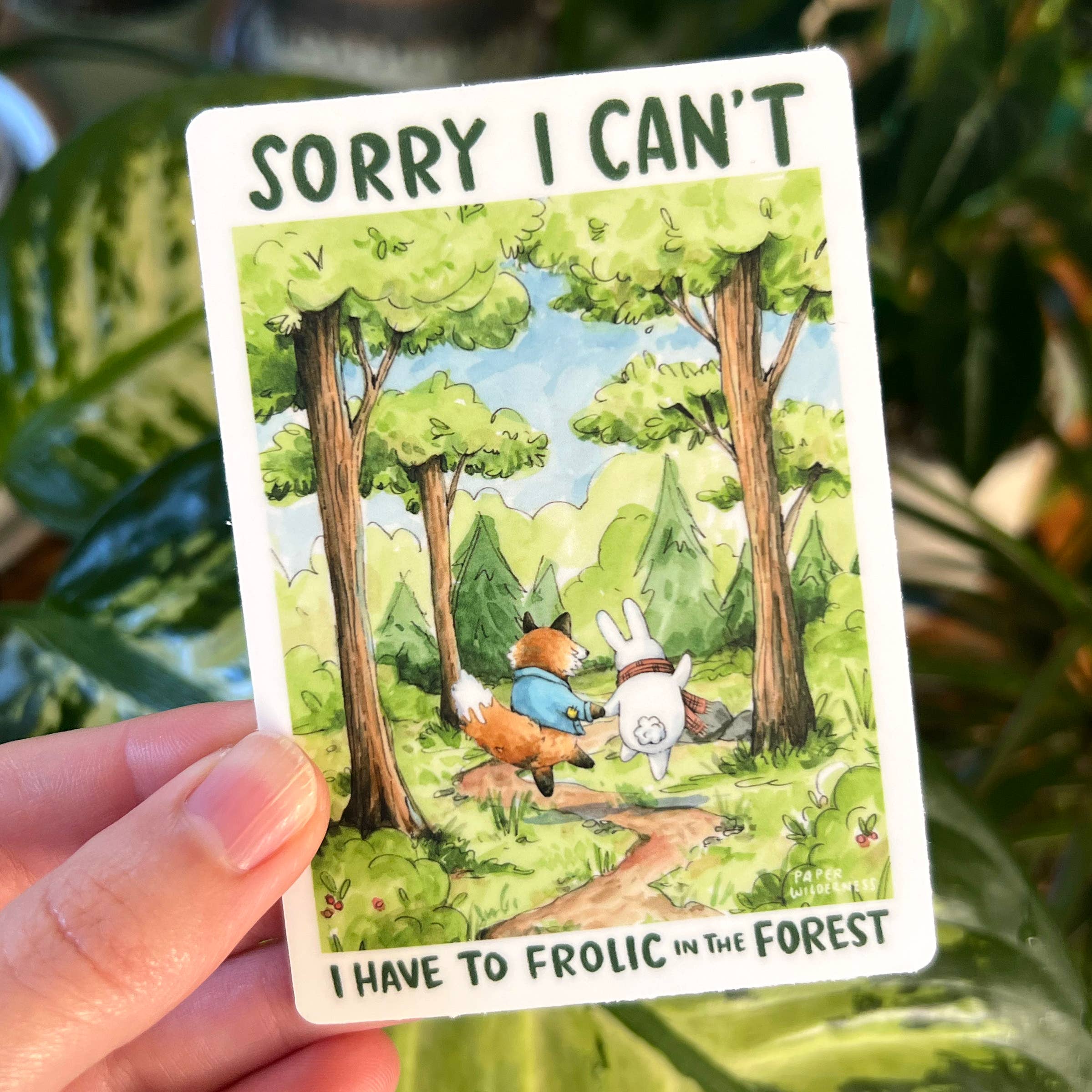 Sorry I Cant I Have To Frolic In The Forest sticker featuring cartoon animals and a forest, held in a hand.