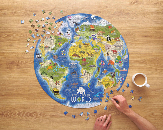 The Endangered World 1000 Piece Jigsaw Puzzle partially assembled on a wooden table next to a coffee cup.