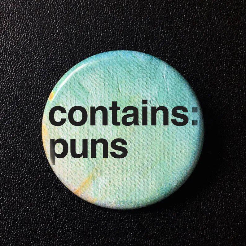 Contains Puns button pin with bold black puns on a light blue background, shown on black leather.