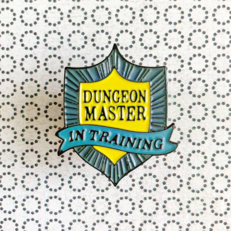 Shield-shaped DM in Training D&D/RPG enamel pin.