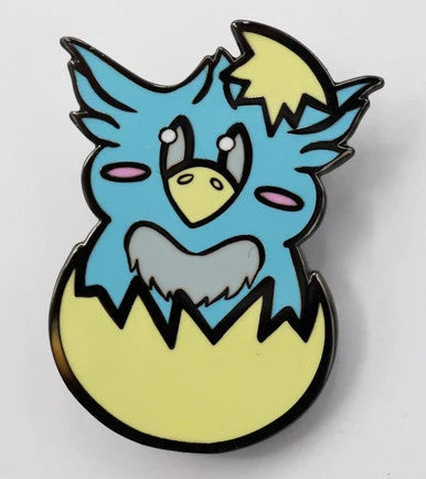 Blue Hippogriff baby monster enamel pin hatching from yellow egg, inspired by Foam Brain Games.