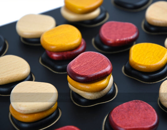 Giant QAWALE colorful wooden pieces stacked on a black strategy board.