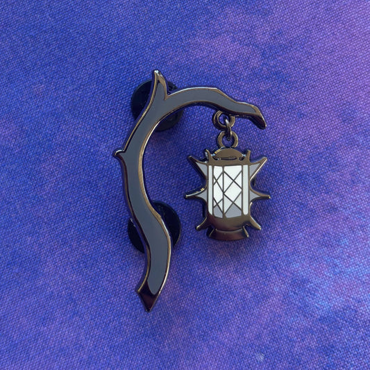 Moonlantern Pin with a black enamel branch holding a glowing lantern on a textured purple background.
