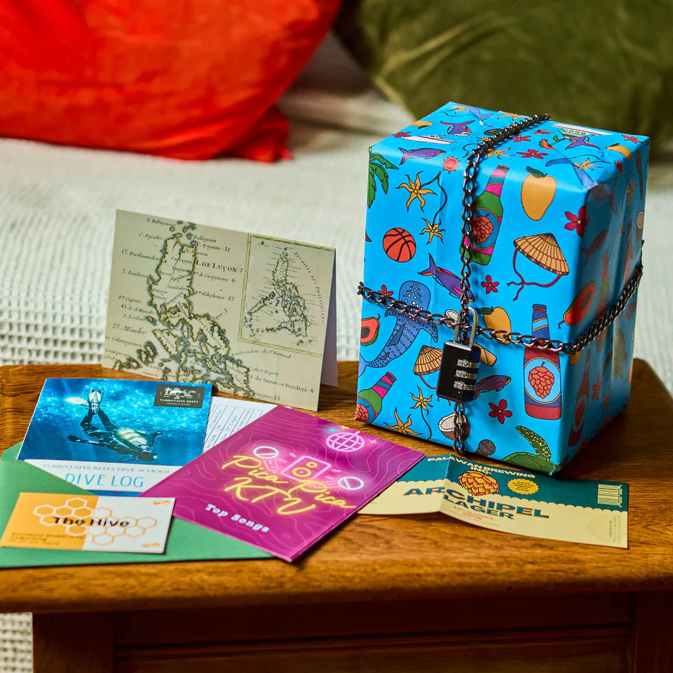 Padlockd The Philippines blue gift box with travel-themed designs, shown with postcards and travel documents.