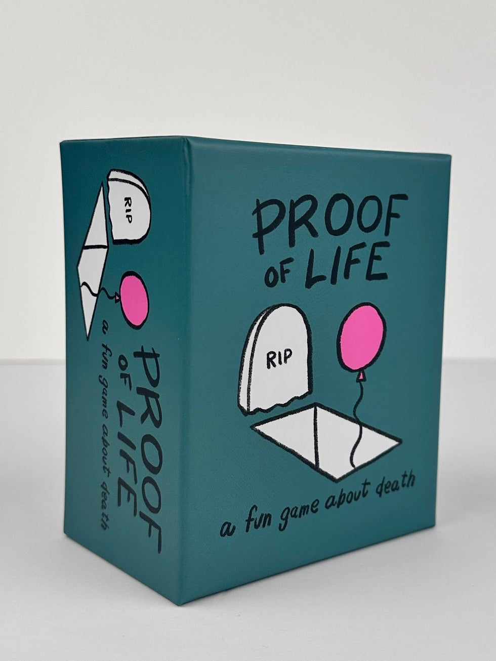 Proof of Life card game teal box, features tombstone, pink balloon, and title text; theme: death and grief.
