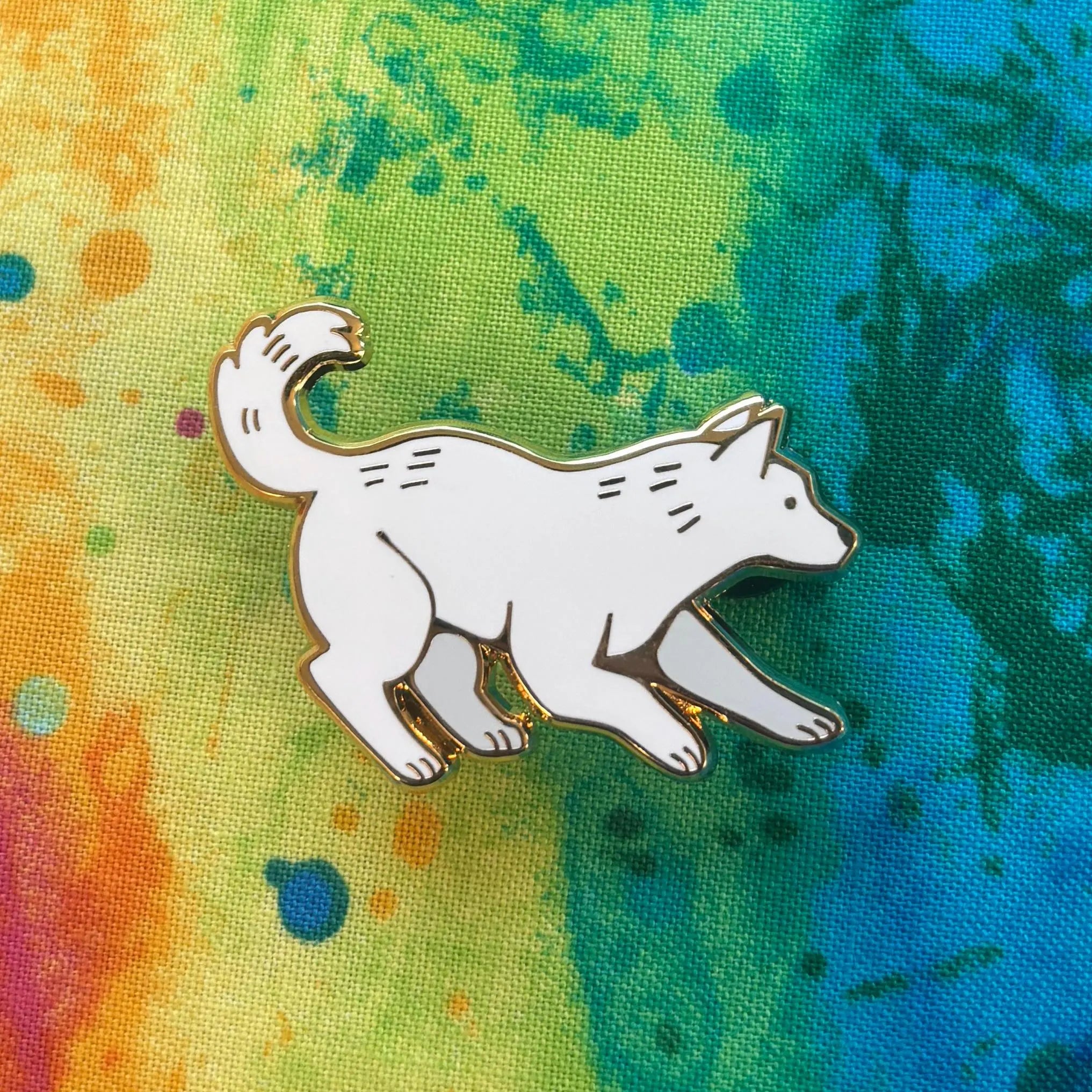 The Scratch Pin featuring a white cartoon dog on a tie-dye background with blue, green, yellow, and orange colors.