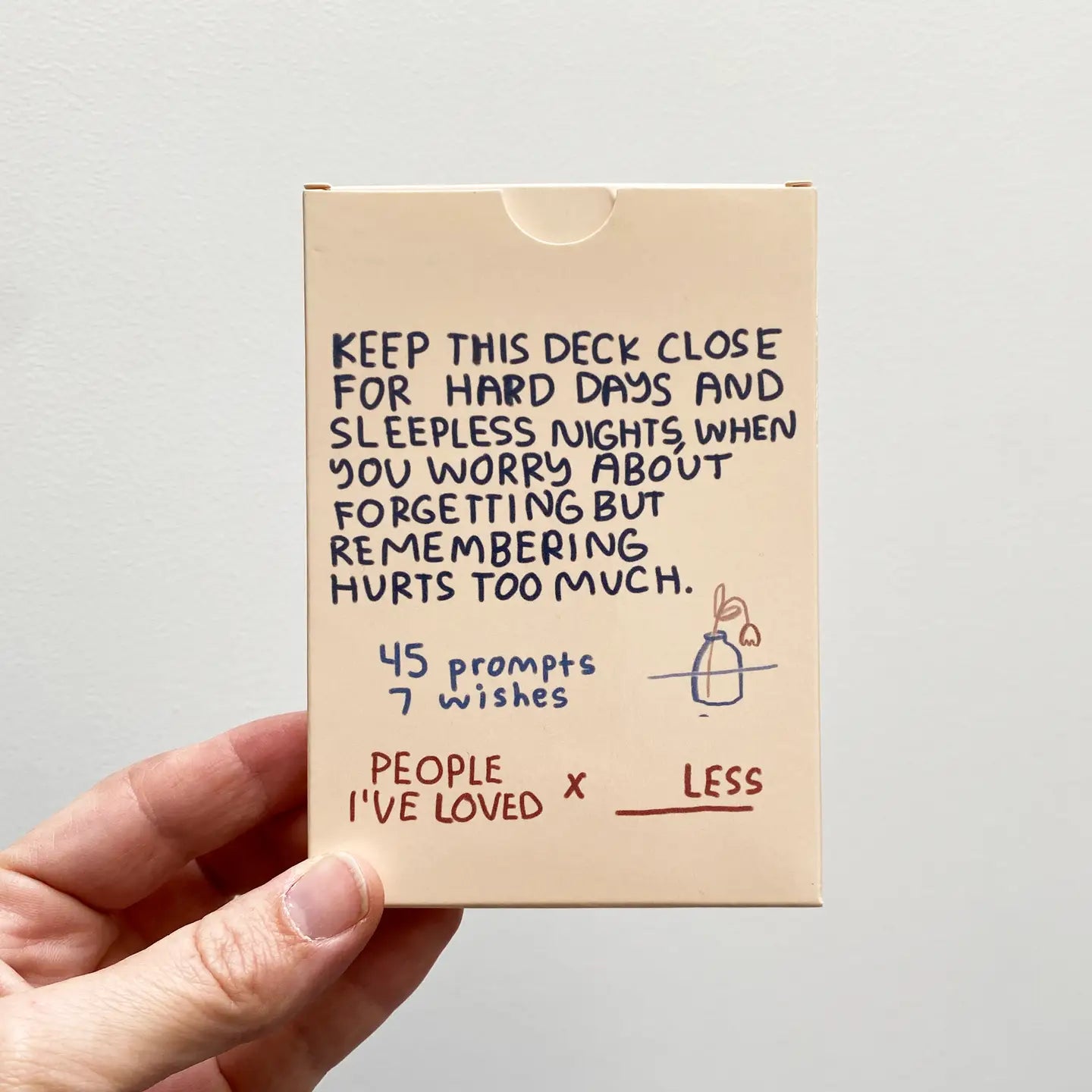 Sitting With Sadness Deck, a set of cards with grief journal prompts, shown held in a hand.