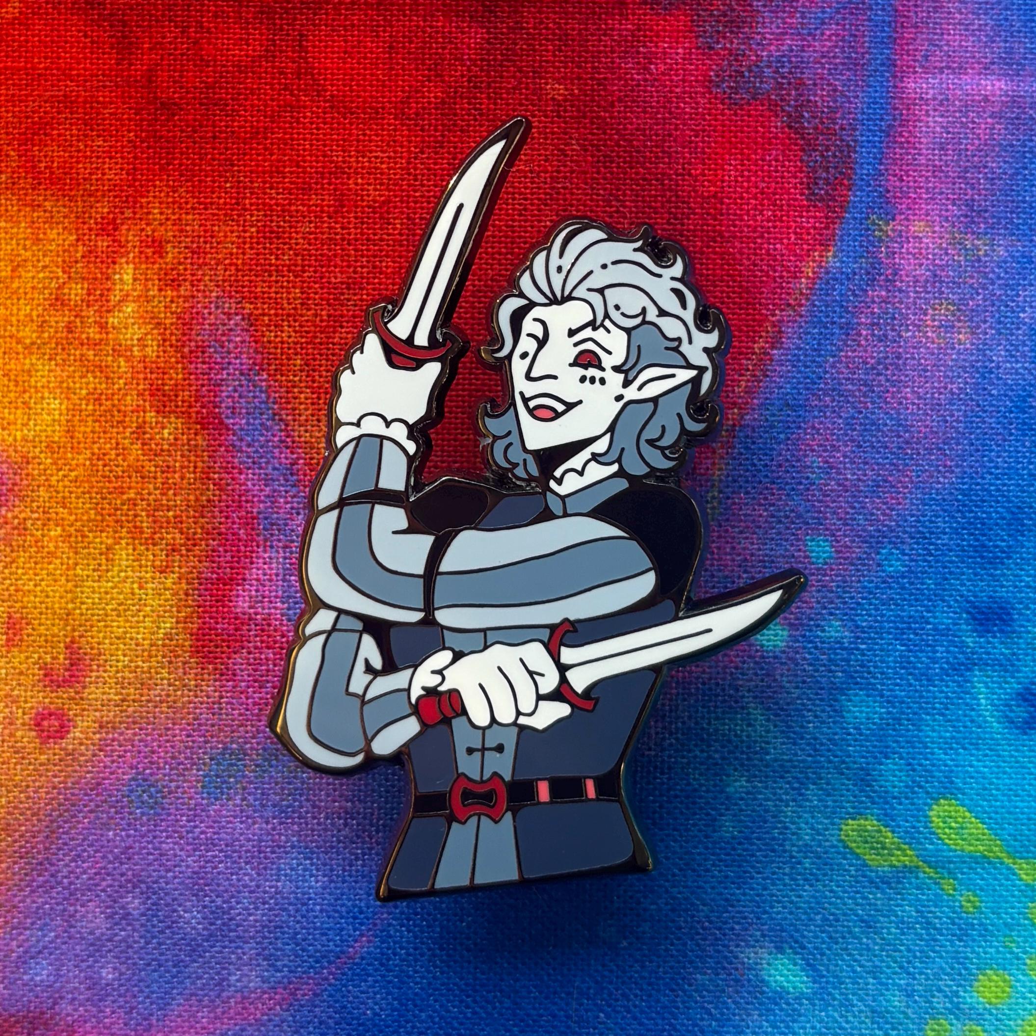 Astarion - Dual Destinies Pin featuring a cartoon elf with gray hair holding two knives, red and blue background.